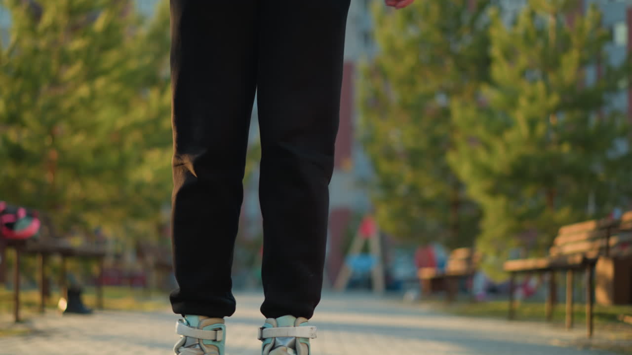 A close-up shot focusing on the lower body of a person wearing black trousers, rollerblading through a park. The scene highlights the casual, outdoor activity with a background of greenery and benches