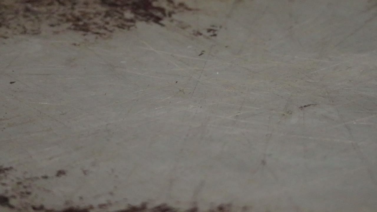 An extreme close up of non stick spray being sprayed onto a well worn baking sheet