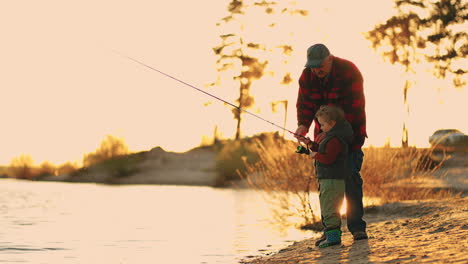 old fisherman and little boy are fishing on shore of river or lake in sunny evening happy family weeknd