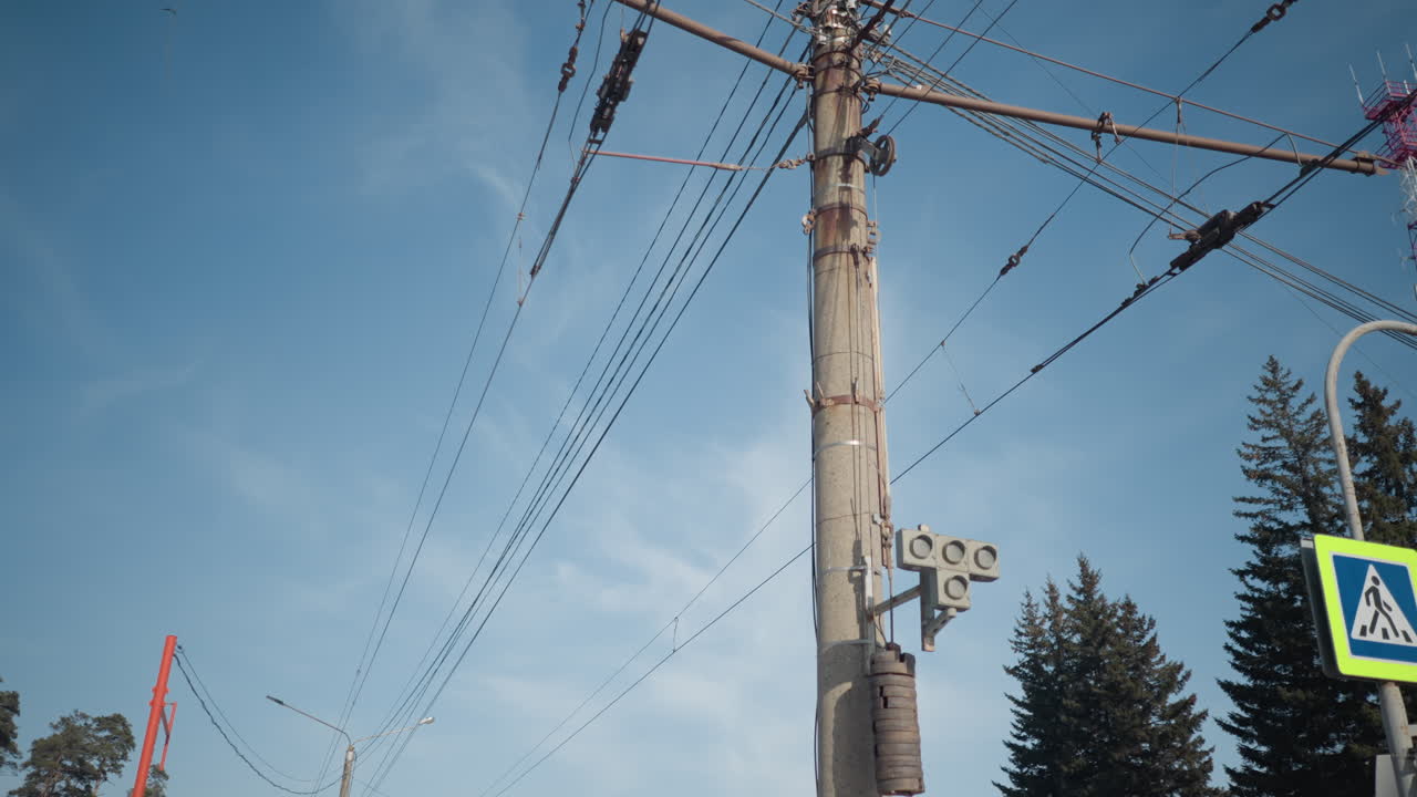urban view shows electric poles, tangled trolley wires, street signs and evergreen trees under bright winter sky, silent transit junction, crisp light, cold season mood around snowy stop