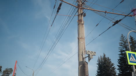 urban view shows electric poles, tangled trolley wires, street signs and evergreen trees under bright winter sky, silent transit junction, crisp light, cold season mood around snowy stop