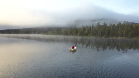 person rowing a boat during a sunrise with misty landscape and trees