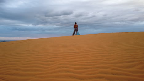 Vista-Posterior-De-Una-Mujer-De-Pie-Sobre-La-Arena-Y-Disfrutando-De-La-Vista-Del-Atardecer-En-Las-Dunas-De-Arena-Roja,-Mui-Ne,-Vietnam