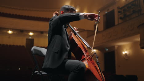 rehearsal of symphonic orchestra in philharmonic hall cellist in black suit is playing cello on scene