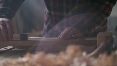 Carpenter measures and marks wood in moody workshop