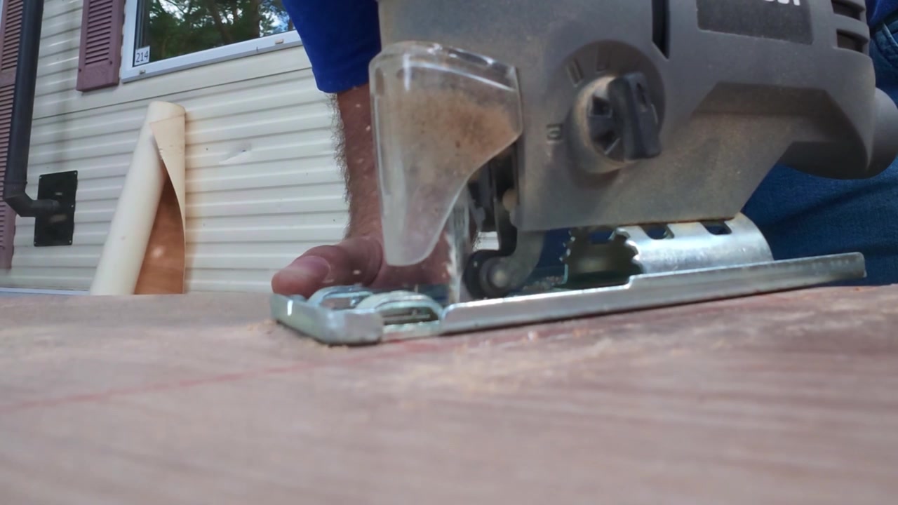 Close-up perspective of an electric jigsaw cutting through white oak laminate flooring planks. Detailed view of the power tool in action during an outdoor home improvement and carpentry project.