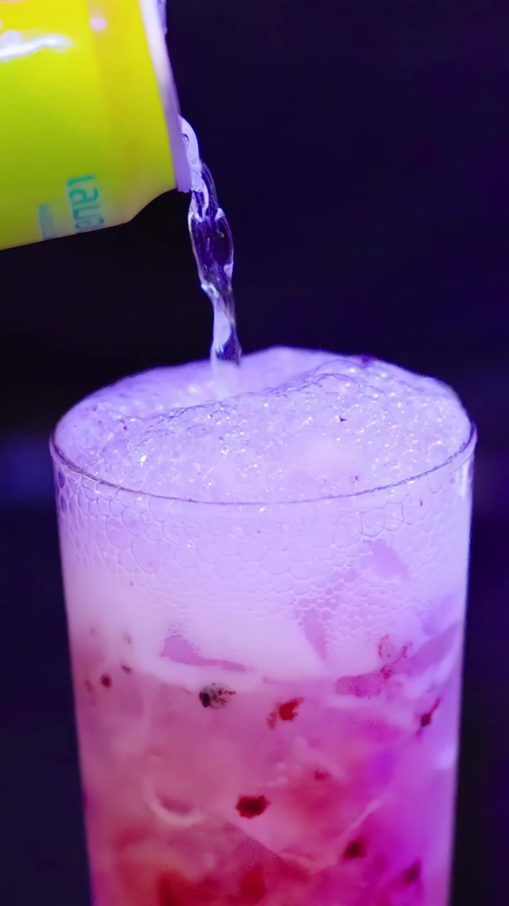 Barman versa soda al limone in un bicchiere da cocktail ghiacciato sotto un'illuminazione vivace, creando bolle schiumose