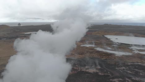 aerial panning shot of a geothermal hot spring billowing steam from the ground