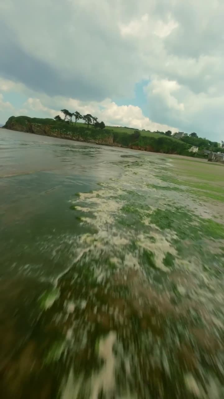 FPV drift across high coastal ridge and homes revealing beach curves, bright sea, and windy open cliffs, vertical