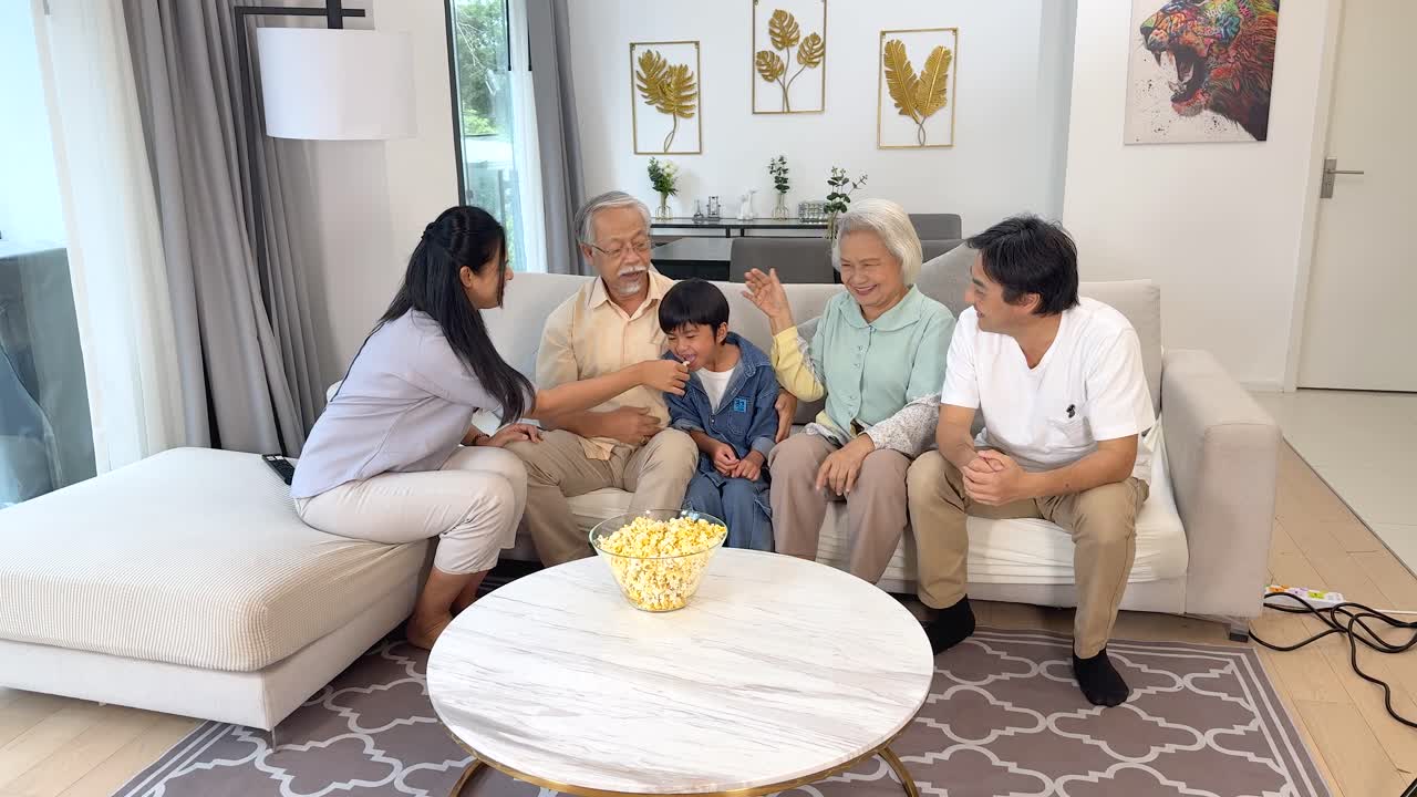Multi-generational Asian family laughing together on sofa in bright, modern living room, natural lighting