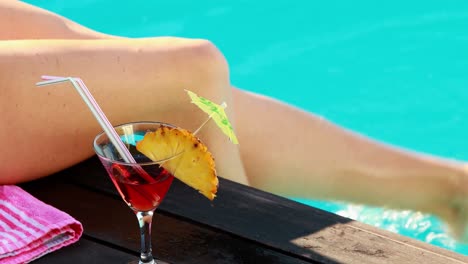 Women-dangling-her-legs-in-swimming-pool-with-cocktail