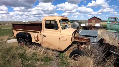 Old-rusty-truck-sitting-in-a-grassy-field-on-a-sunny-day-during-the-summer-with-a-blue-sky-and-clouds-overhead