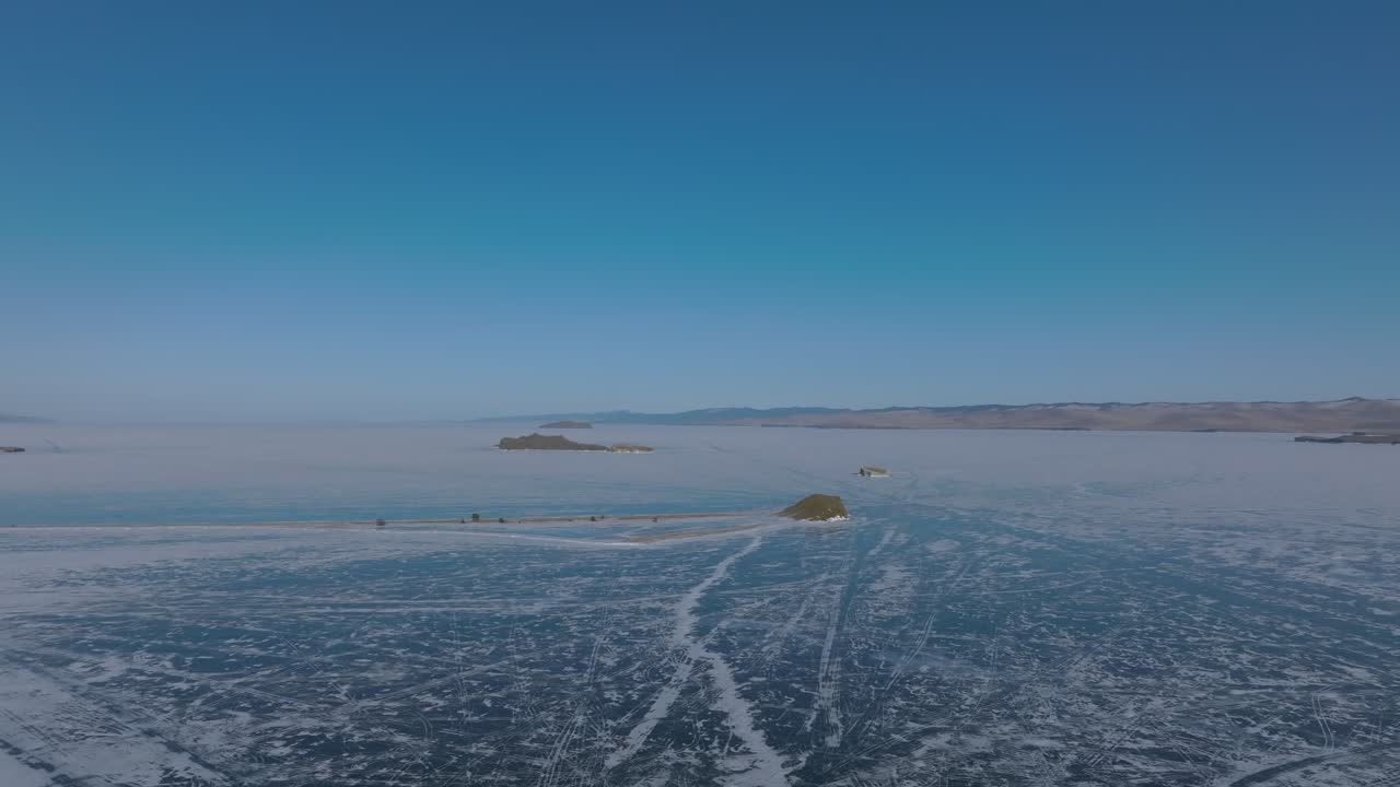 Droneoptagelser af det frosne Maloje More-stræde på Bajkal-søen med små klippeøer, snemønstre og isrevner under en klar blå himmel, Irkutsk oblast, Rusland