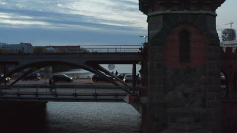 Bikers-and-Car-traffic-on-Berlin-Oberbaum-Bridge-old-famous-building-over-Spree-River-in-evening,-Aerial-Follow-Slide-right