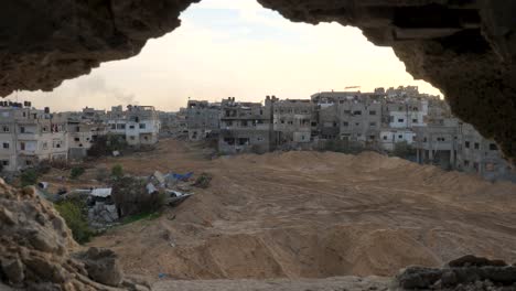 reverse reveal of a hole in the wall while looking towards a destroyed gaza city block