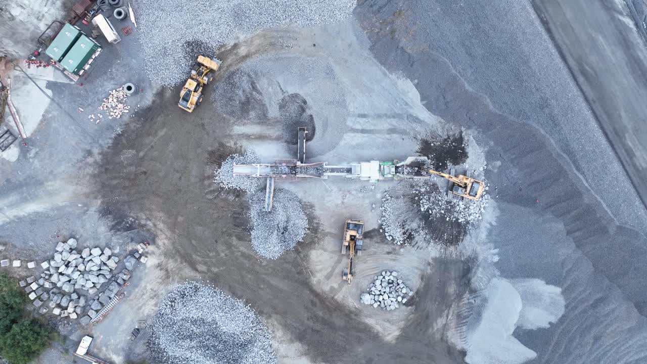 Drone shot of conveyer belt and bob cat sorting rocks and rubble into piles in quarry mine