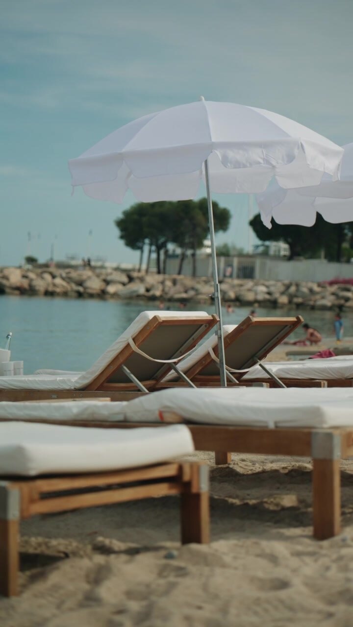 Eleganti lettini da spiaggia e ombrelloni bianchi in riva a un mare tranquillo durante una soleggiata giornata estiva.