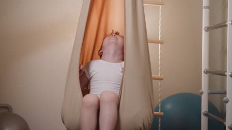 Relaxed-little-boy-swaying-in-beige-hammock-hanging-in-gym