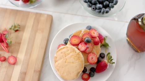 overhead view of pancakes with fruits and honey in kitchen, slow motion