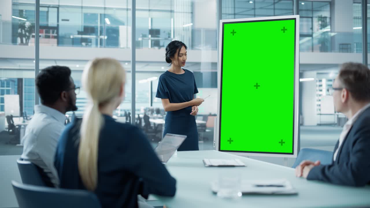 여성 운영 관리자는 경제학자 팀을 위해 회의 프레젠테이션을합니다. 아시아 여성은 수직 녹색 화면 모의 디스플레이와 함께 디지털 화이트보드를 사용합니다. 사람들은 비즈니스 사무실에서 일합니다.