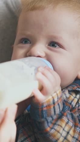 careful mother feeds little baby with milk from bottle in spacious light room on sunny day close view