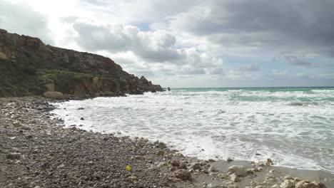 piles of rocks on a golden bay beach with mediterranean sea waves crashing on sandy shore