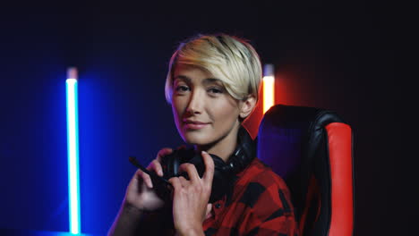 young woman sitting at desk and looking at camera in a room with colorful neon lamps on the wall