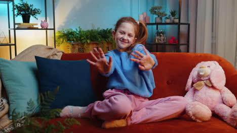 child kid girl smiling friendly at camera waving hands gesturing hello hi greeting at home on couch