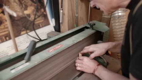 woodworker using industrial belt sander to smooth circular wood piece