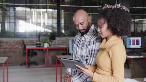 Two-happy-diverse-creative-designers-in-discussion-at-tablet-in-casual-office,-slow-motion