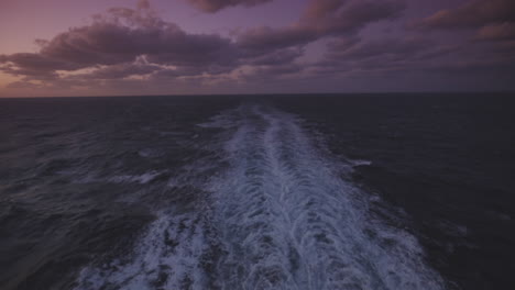 outside deck with lanterns at a cruise ship with a propeller wash in the calm sea on a partly cloudy dusk. dolly wide shot