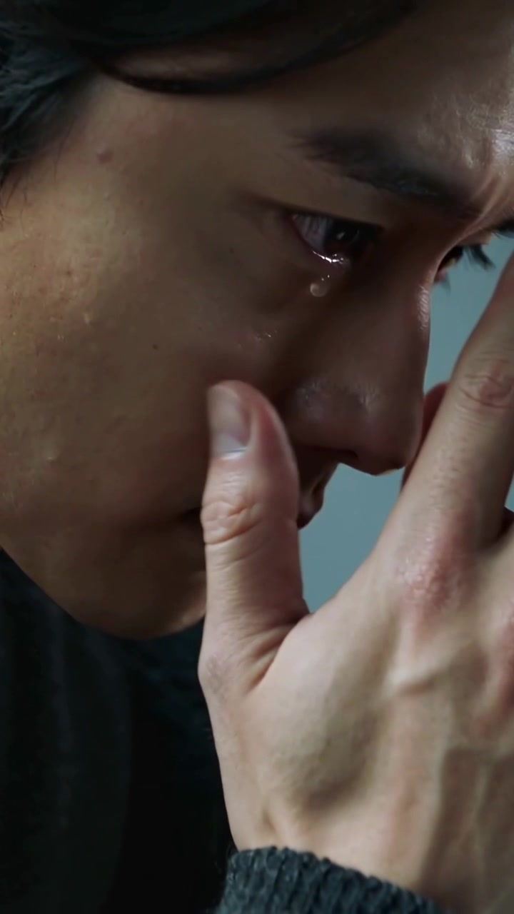Vertical video: Sad Asian man pressing fingers to cheek, wiping tear in studio, ribbed cuff