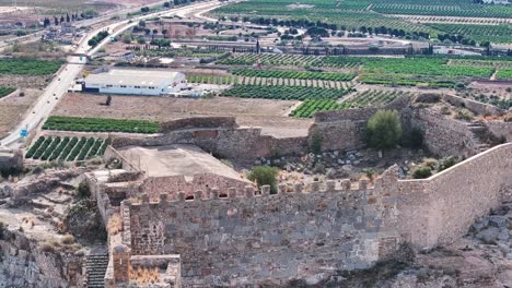 flight where we see a part of the castle where they keep archaeological remains and in the background there are orange tree crops and some roads with vehicles circulating we see a parallax effect