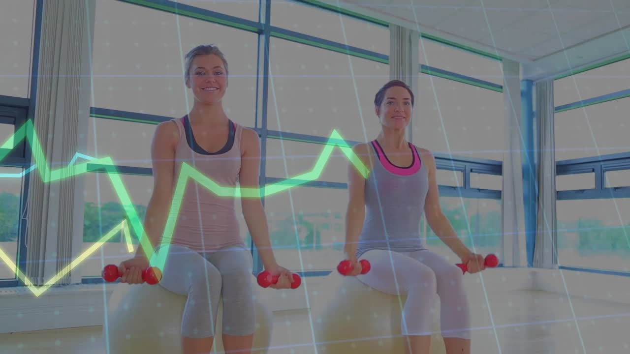 Two women performing bicep curls on stability balls in fitness studio, overlaying neon line graphs