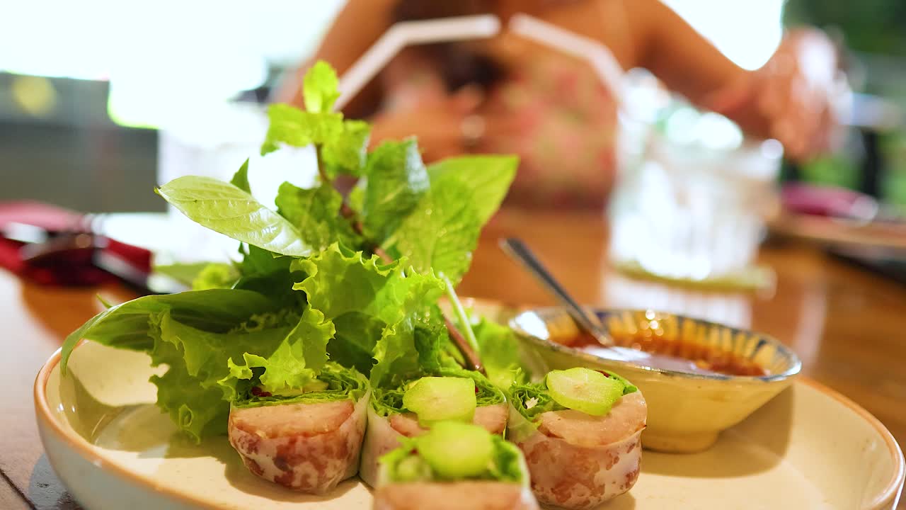 A plate of fresh Vietnamese food with herbs and dipping sauce on a wooden table in a well-lit restaurant