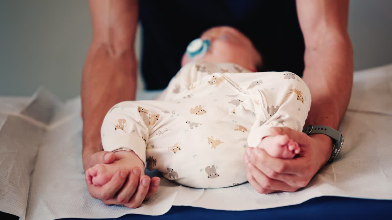 Close up of an infant's legs and feet while caregivers gently reposition the baby during a care or examination session