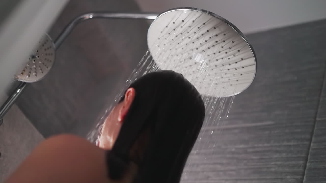 la señora está bajo el suave flujo de agua caliente. la mujer bajo la gran cabeza de ducha disfrutando de la sensación de lavarse como un cómodo abrazo. la ducha alivia el estrés