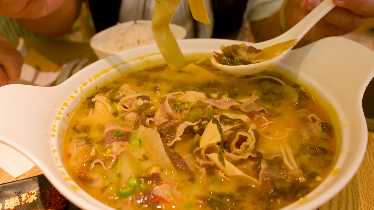 Primo piano statico di mani che usano bacchette e cucchiaio per mangiare una zuppa di manzo asiatica piccante