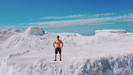 sporty man with muscular body on the top of white hill under blue sky. handsome sportsman on beautiful summer landscape in the mountains. motion down.