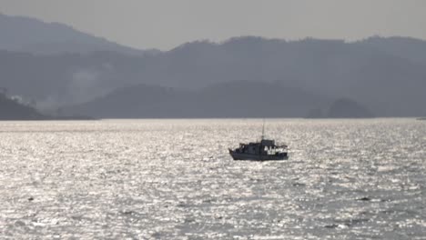 Un-Barco-Pesquero-Navegando-En-El-Océano-En-Un-Paisaje-Parecido-A-Una-Península-Con-Montañas-Y-Una-Costa-Al-Fondo