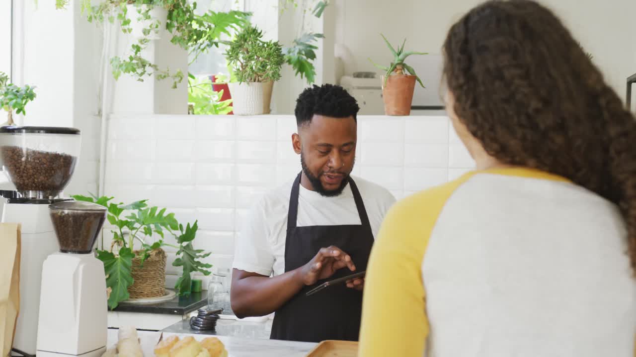 Happy african american male barista taking order from biracial female client at cafe