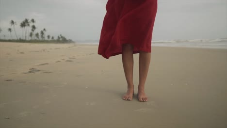 Eine-Intime-Aufnahme-Am-Strand-Konzentriert-Sich-Auf-Die-Nackten-Füße-Eines-Mädchens,-Das-Elegant-In-Ein-Langes-Rotes-Top-Gekleidet-Ist