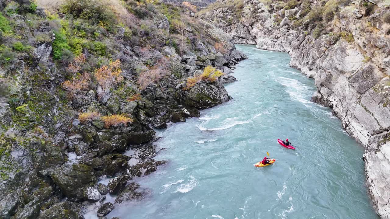 Two kayakers navigate the rapids of Kawarau River in Queenstown, New Zealand, surrounded by rugged cliffs and vibrant foliage