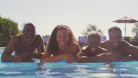 Multi-Generation-Family-With-Adult-Offspring-On-Summer-Holiday-On-Inflatable-In-Swimming-Pool