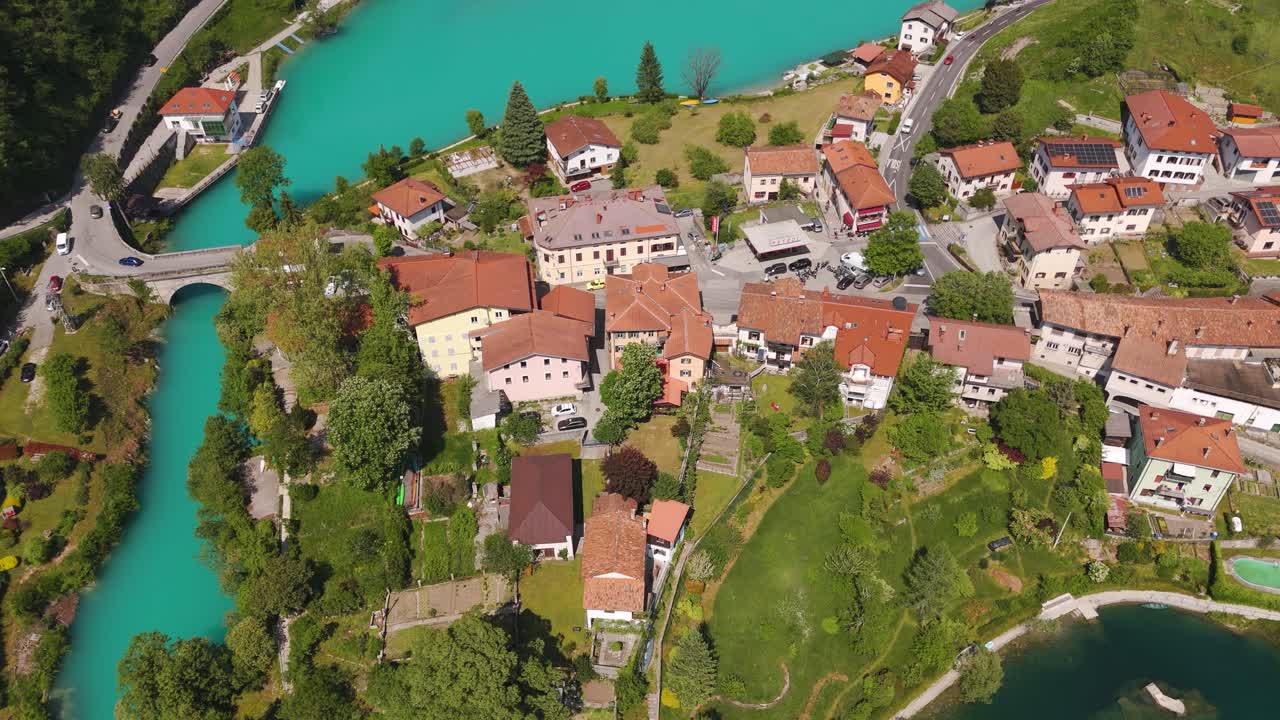 Aerial establishing drone fly houses next to a blue lake in Drone Flyover of Most na Soči and Soča River in Posočje Valley during summer