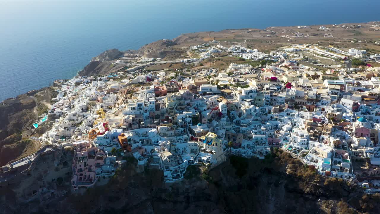 Oia with white cave houses and villas from aerial top down view revealing cliffs during sunset in Santorini, Greece.