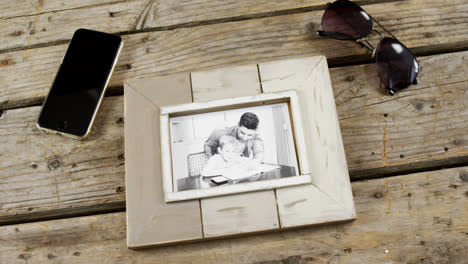 photo frame, sunglasses and mobile phone on wooden plank