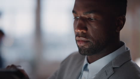 young african american businessman using tablet computer working late in office browsing information looking at data on digital touchscreen