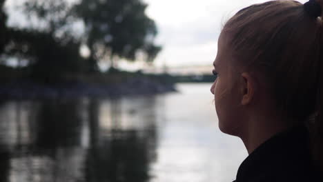 young girl sitting on a lake coast and staring at the water