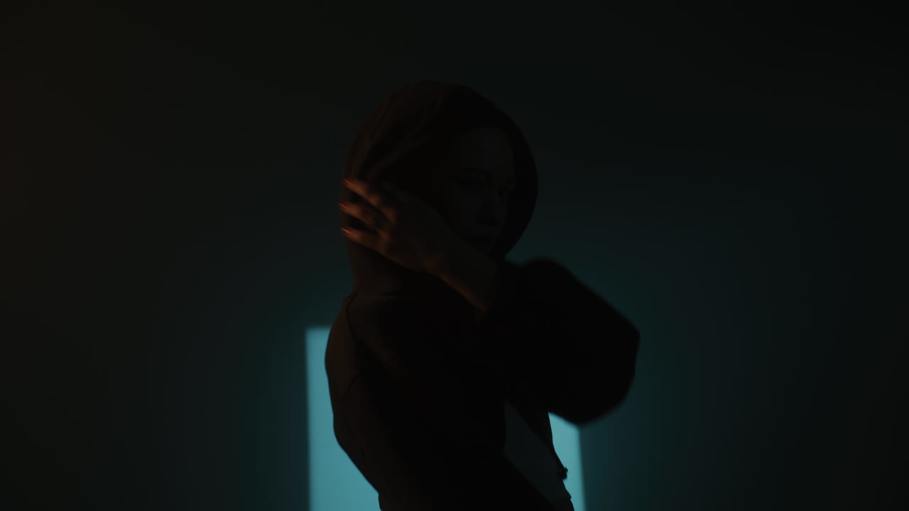 Silhouette of a person wearing a hoodie in a dark room